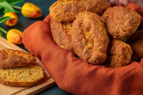 Fresh potato rolls in a basket with orange cloth, one cut open