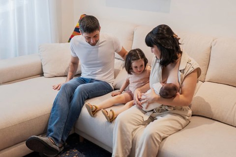 A young family enjoys a tender moment at home with their newborn baby. The big sister looks on with