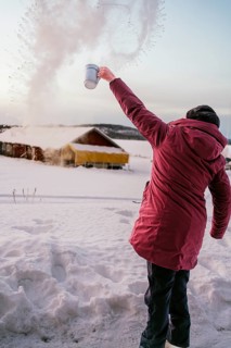 A person in a red coat throws water into the frigid air in Swedish Lapland, creating an impressive