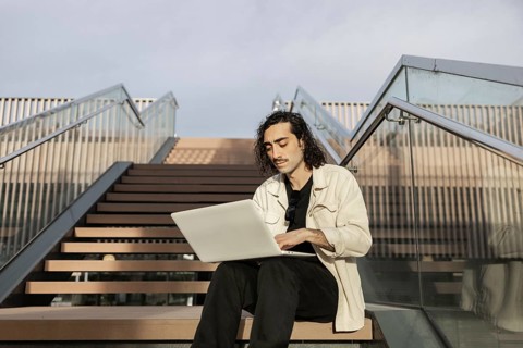 A man sits on outdoor steps, focused on his laptop He embraces a modern, flexible working