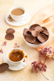 Chocolate chips with cup of coffee and caramel on a beige concrete background and orange textile.