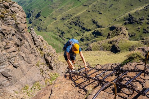 Young female hiker climbs over dangerous ladders, mountains and cliffs of the Drakensberg