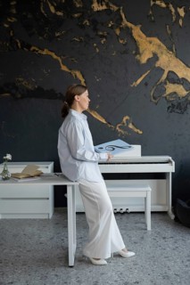 Woman sitting at a table with a piano and open music book, preparing piano lessons. The setting is