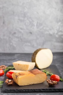 Smoked cheese and various types of cheese with rosemary and tomatoes on black slate board on a