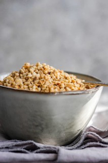 A bowl filled with chopped hazelnuts rests on a textured gray napkin, accompanied by an antique