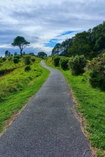 A tarmac path leads through a green and hilly landscape under a partly cloudy sky, Cathedral Cove,