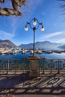 Lantern, forged railing, lakeside promenade, shadow, marina, trees, motorboats, hill with village,
