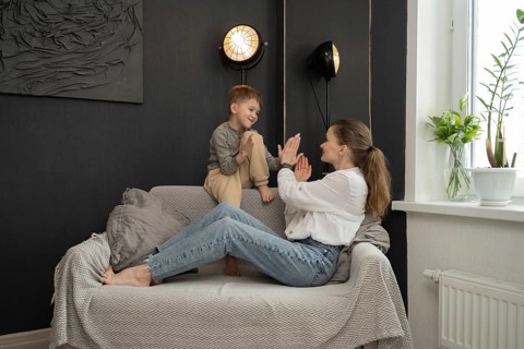 Mother and son share a joyful bonding moment on the couch, surrounded by cozy home decor. The boy