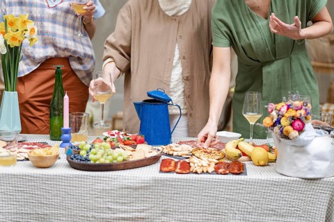 A casual gathering features coworkers enjoying wine and appetizers around a decorated table.
