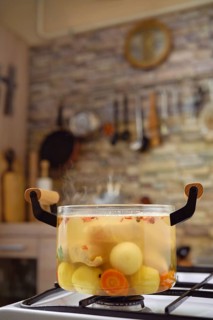 A pot filled with fresh vegetables and fish is simmering on the stove, releasing steam into a cozy