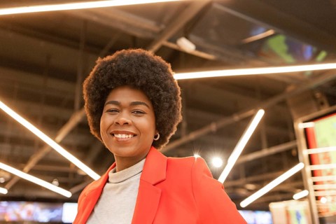 A smiling woman wearing a red blazer stands confidently in a contemporary setting with geometric