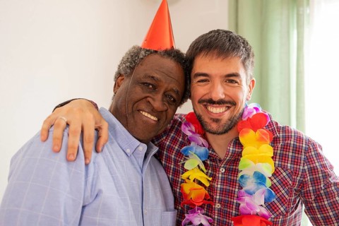 Two people celebrating a birthday, wearing festive attire with a colorful lei and party hat. They