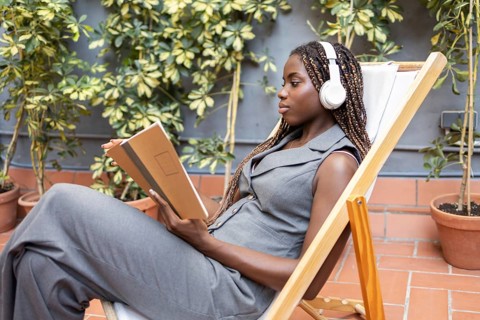 A young African woman with braids listens to music on headphones while relaxing with a notebook in