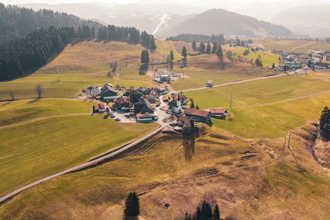 A village is surrounded by green meadows and gentle hills, surrounded by mountains, Oberreute,
