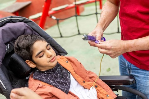 A child with cerebral palsy in a wheelchair receives feeding assistance through a tube at an