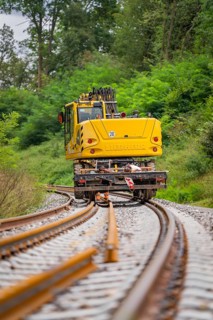 Yellow construction equipment working on railway tracks in the middle of a green landscape, track