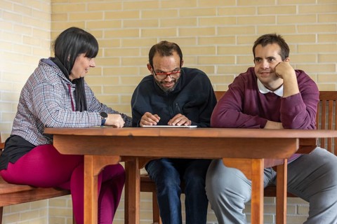A supportive caregiver interacts with two residents at a mental health residence, sharing a moment