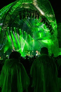 Audience in rain ponchos at a night concert in front of a green-lit stage, Klostersommer, Calw