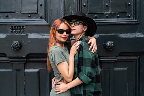 A Colombian lesbian couple embraces, showcasing pride and love against a rustic backdrop,
