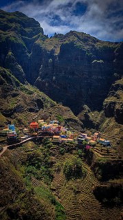 Panoramic view, small settlement, colorful village, nestled in raw, dramatic mountains under blue