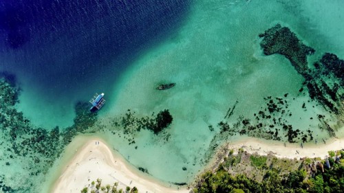 An aerial view captures two boats floating on the clear, turquoise waters near a white sandy beach