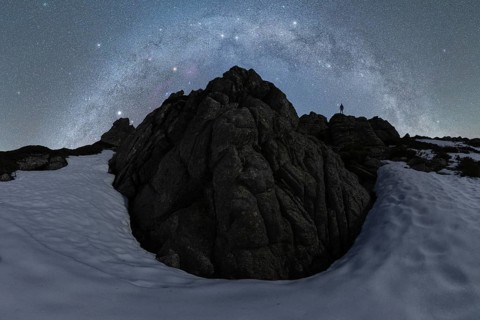 A stunning view of the Milky Way over rugged rocks and snow in Iceland The silhouette of a lone