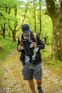 A young father with a yellow backpack walking with the newborn child in the backpack on a path in