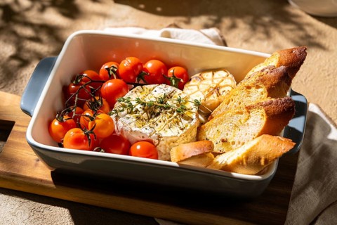 A delectable baked Camembert cheese served with roasted cherry tomatoes and crunchy bread slices.