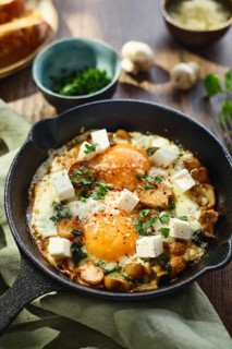 Fried eggs with spinach, mushrooms, grated cheese and feta cheese in small cast iron skillet, close