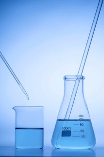 A laboratory beaker and flask filled with blue liquid, with a pipette dripping a drop in. The setup