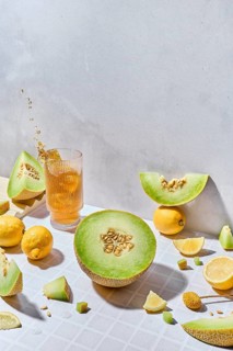 Fresh melon and lemon slices and fresh juice in a glass arranged creatively on a light, textured
