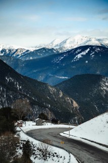 A tranquil winter mountain scene with a winding road, surrounded by snow capped peaks and evergreen