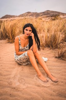 Caucasian brunette in a white floral dress, sitting on the beach of Cabo de Gata, Nijar. Andalucia,