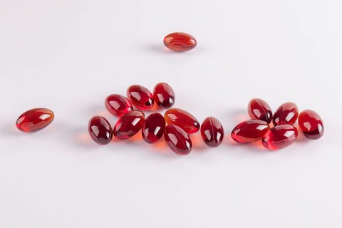 Close-up of vivid red jelly capsules containing omega 3 and vitamin E, arranged on a white surface,