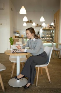 A woman in professional attire sits alone at a cafe table, engaging with a digital tablet.