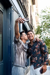 A cheerful latin gay couple takes a selfie while walking in the vibrant streets of Madrid,