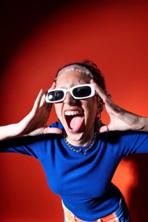 A trendy woman in colorful trousers, tooth gems and white sunglasses poses energetically against a
