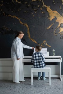 A young student receives piano instruction from a teacher in a cozy home setting. The child sits at