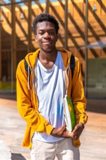 Vertical portrait of an african smiling student standing outside the university under the sun