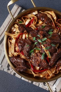 Udon noodles with Mongolian beef, green onions and vegetables, in a brass pan, on a gray