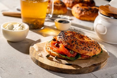 A freshly baked sesame seed bagel topped with smoked salmon, capers, and cream cheese on a rustic