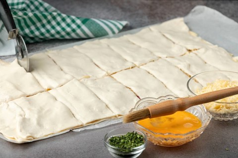 Puff pastry is cut and coated with egg, preparing for baking in the kitchen