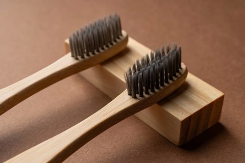 Two bamboo toothbrushes are placed on a wooden block against a warm brown background. These