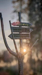 Rennsteig signpost in the frosty forest, illuminated by soft evening light, winter hiking on the