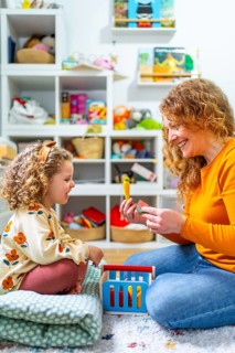 Vertical photo of a cute girl and mother playing with toys in the bedroom together