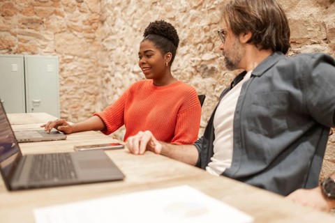 Two professionals collaborate in a warm coworking space, focusing on laptops and discussions The