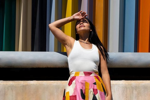 A stylish woman in a colorful outfit stands against a backdrop of modern architecture, creating a