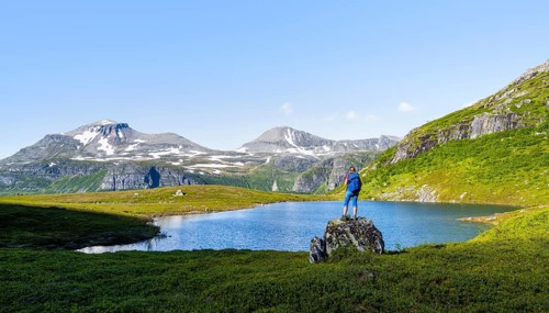 Female hiker standing on a rock in front of a mountain landscape, small lake in the Flatvaddalen