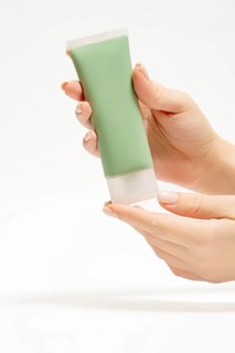 Cropped unrecognizable person holding a tube of green face mask, designed for detox and acne