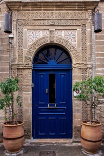 A blue door with ornate rustic patterns and two potted plants next to it, Essaouira, Morocco